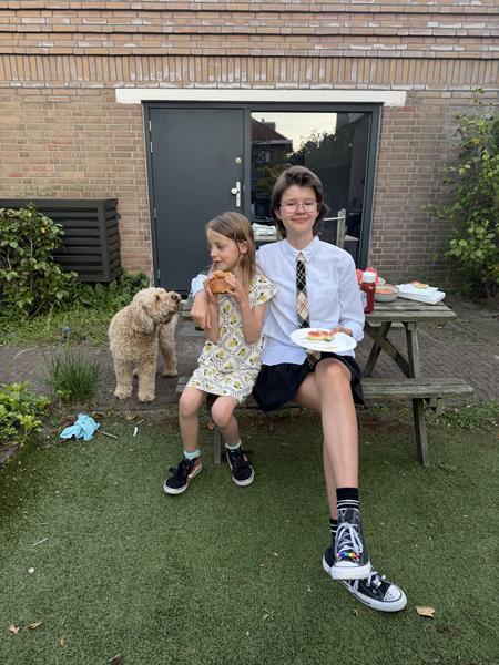 Two girls and a dog are enjoying a casual meal outdoors on a picnic table in the backyard